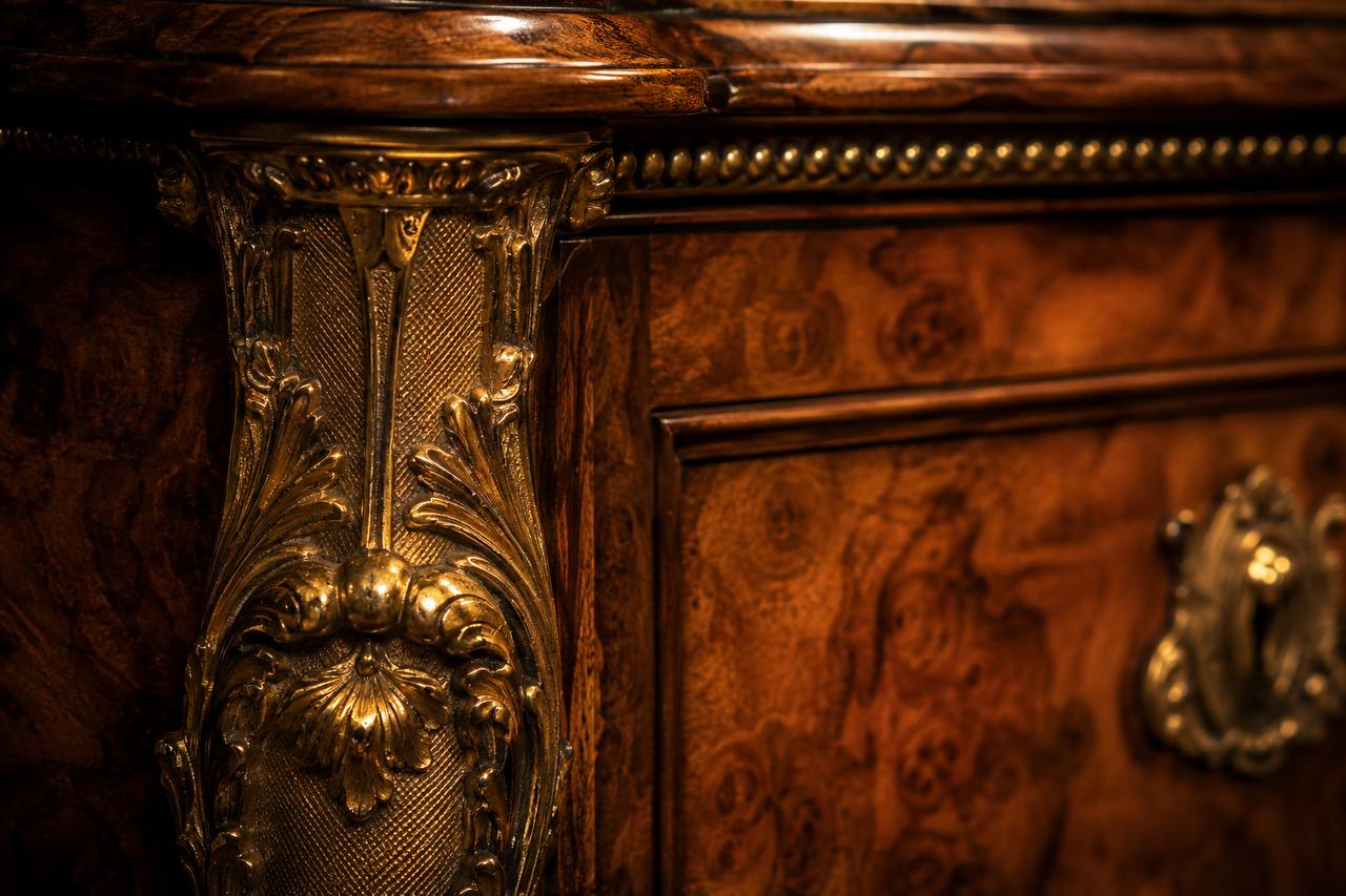Close-up detail of gilt bronze ormolu mount on burr walnut furniture, showing acanthus leaf carving and cross-hatched ground
